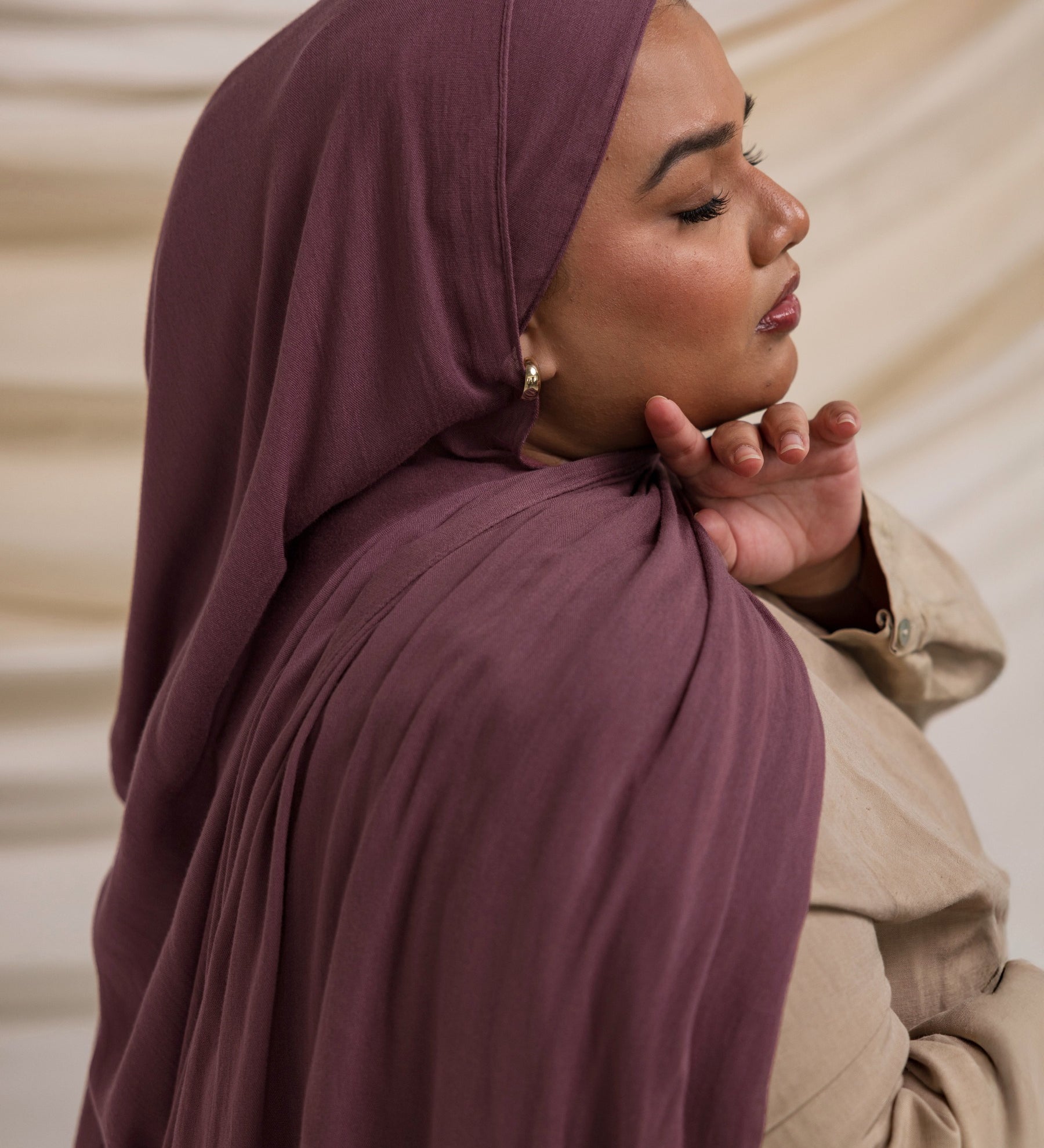 A person wearing a rose colored hijab, matching with a neutral outfit, in a soft lighting environment.