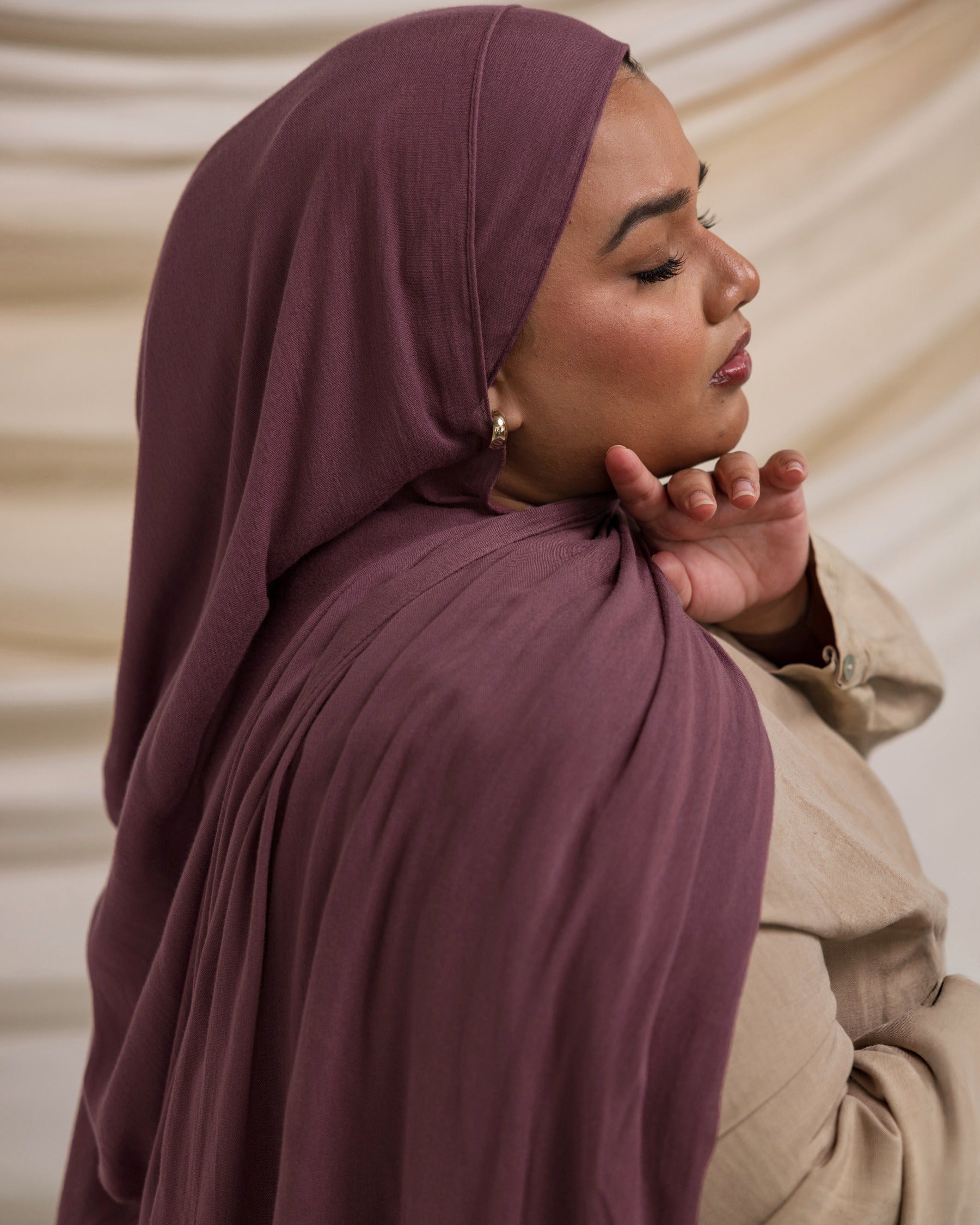 A person wearing a rose colored hijab, matching with a neutral outfit, in a soft lighting environment.