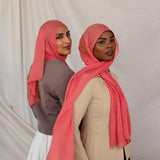 Two women wearing pink coral hijabs against a plain background