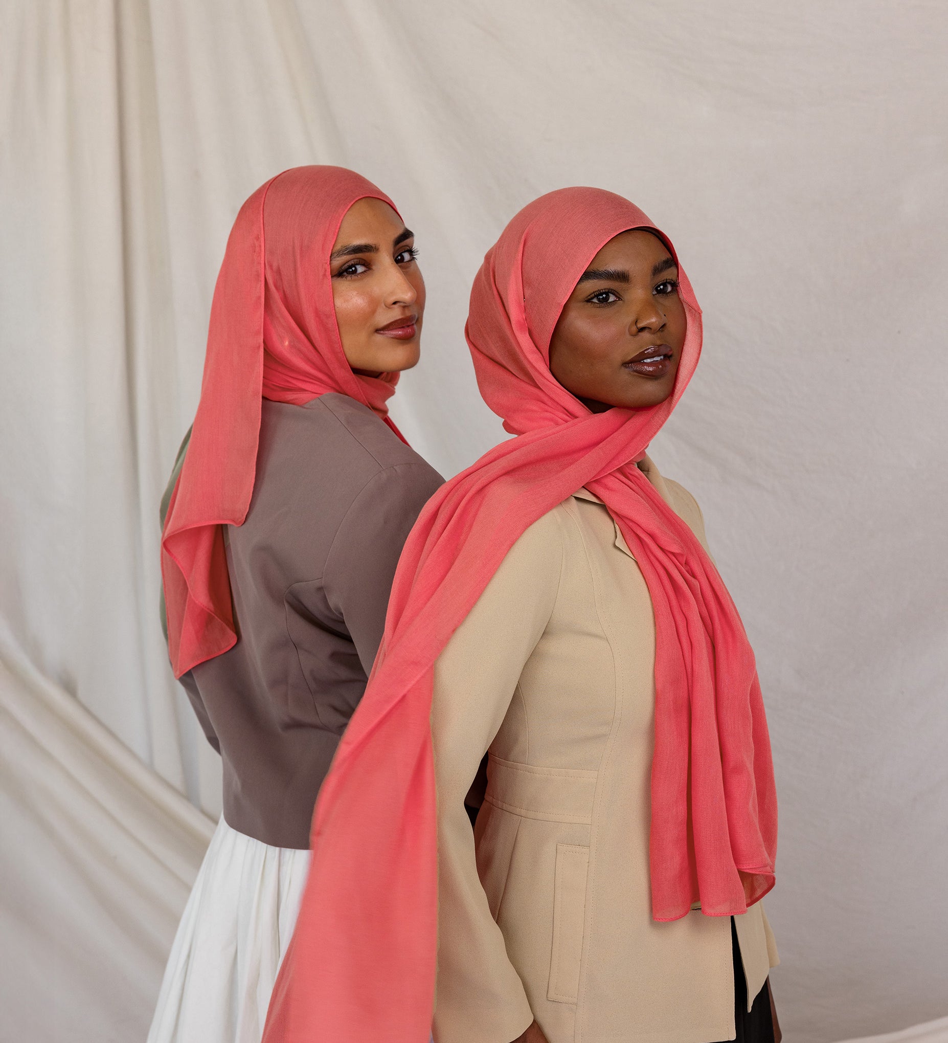 Two women wearing pink coral hijabs against a plain background