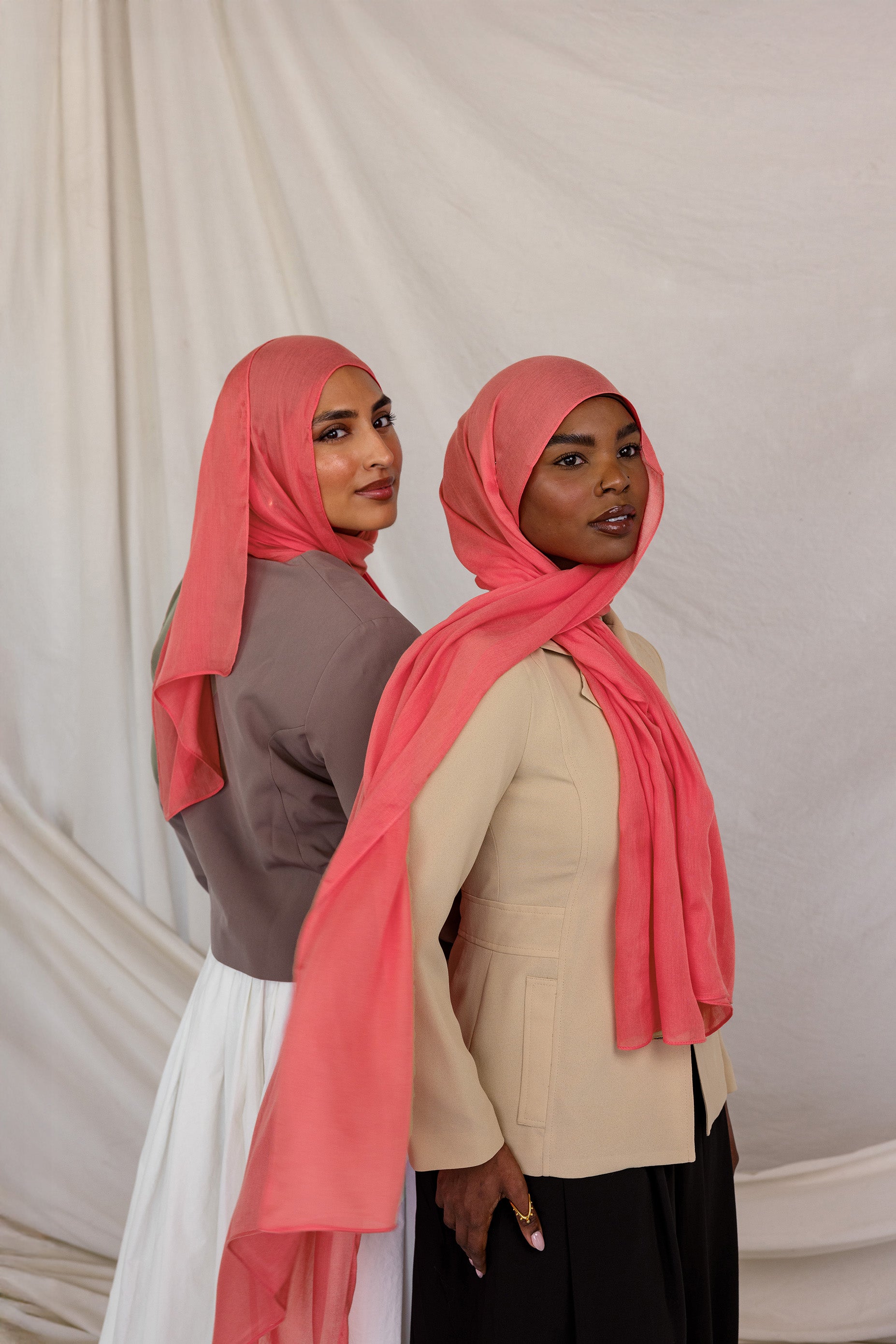 Two women wearing pink coral hijabs against a plain background