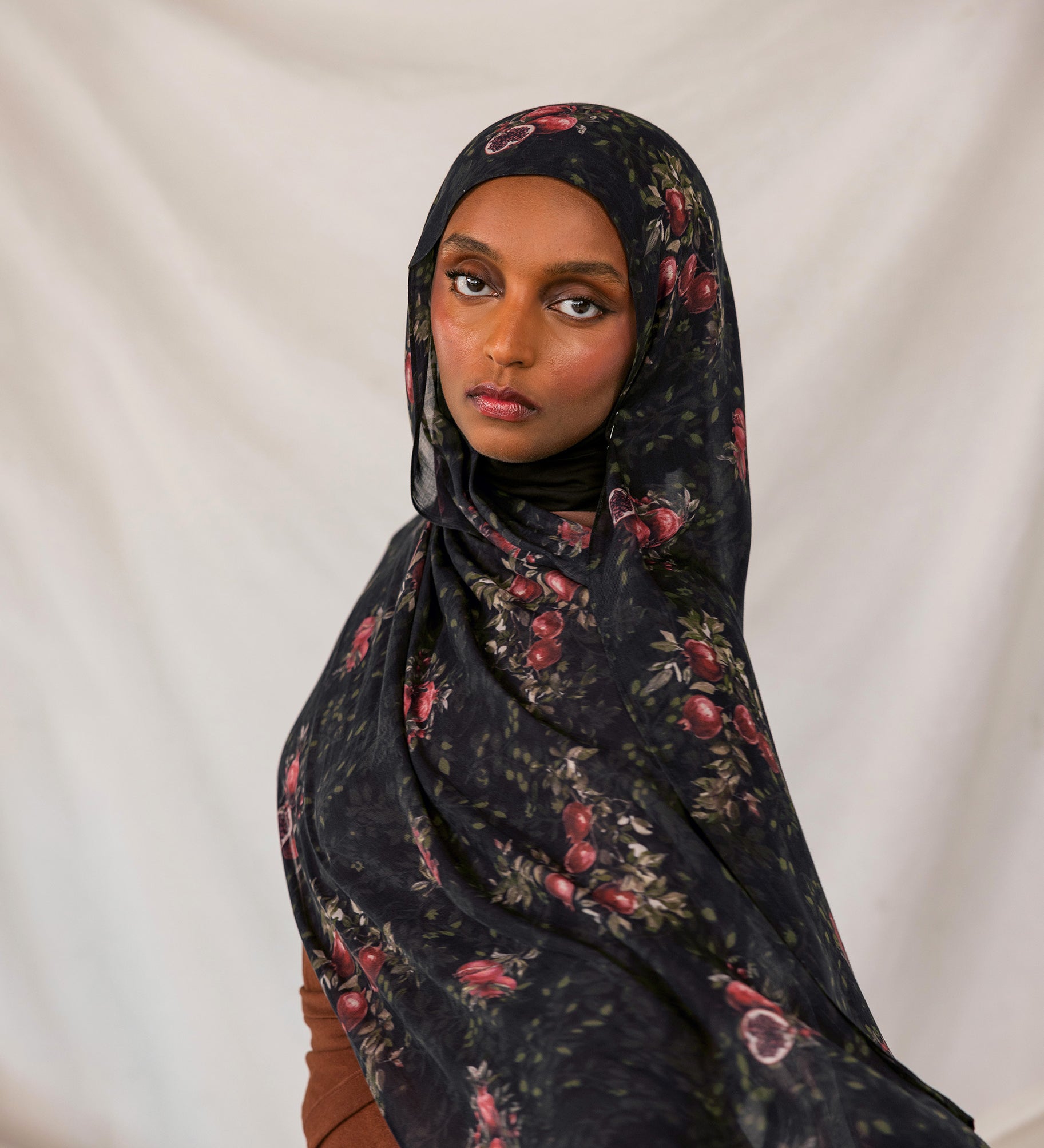 Woman wearing a dark pomegranate hijab against a plain background