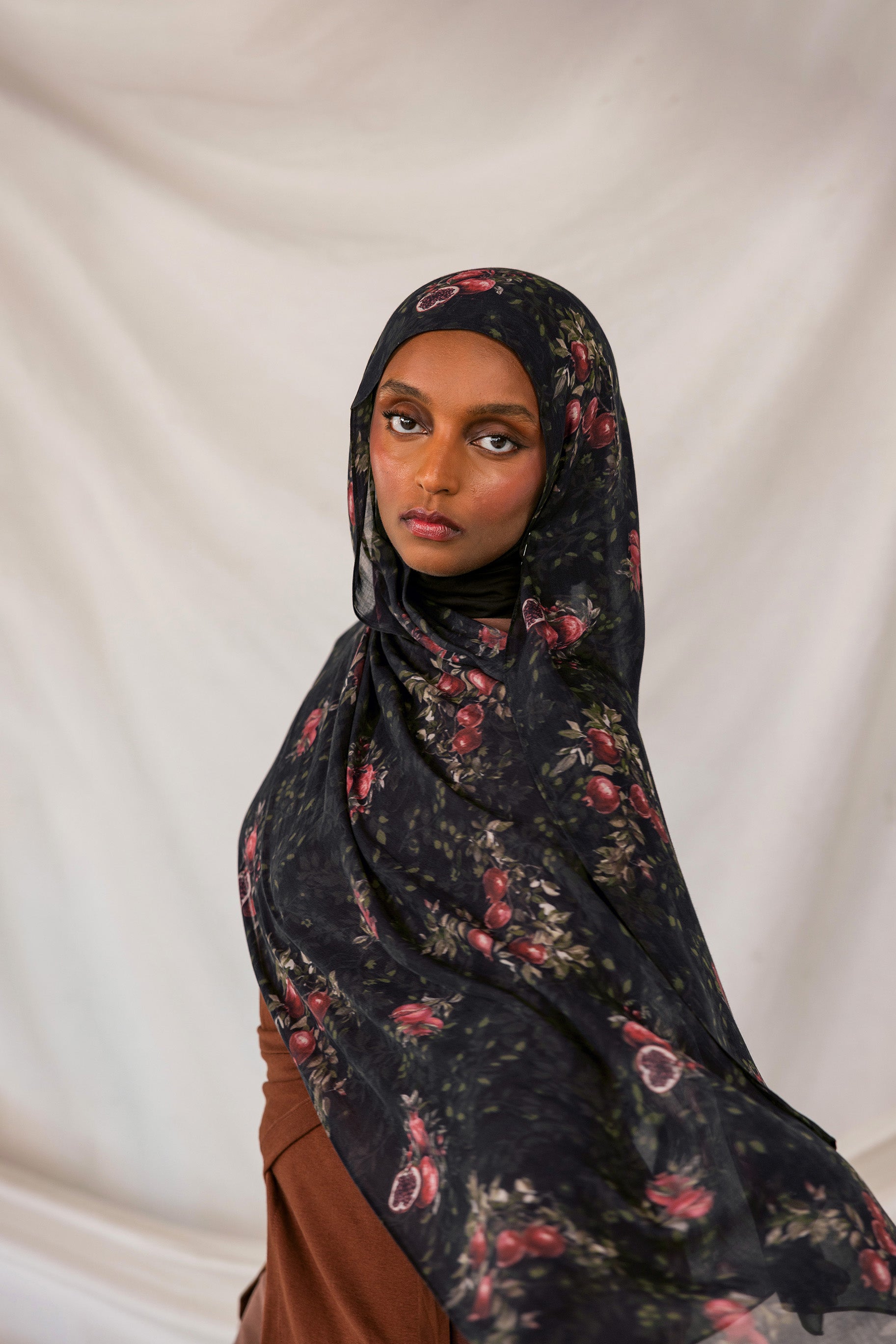 Woman wearing a dark pomegranate hijab against a plain background