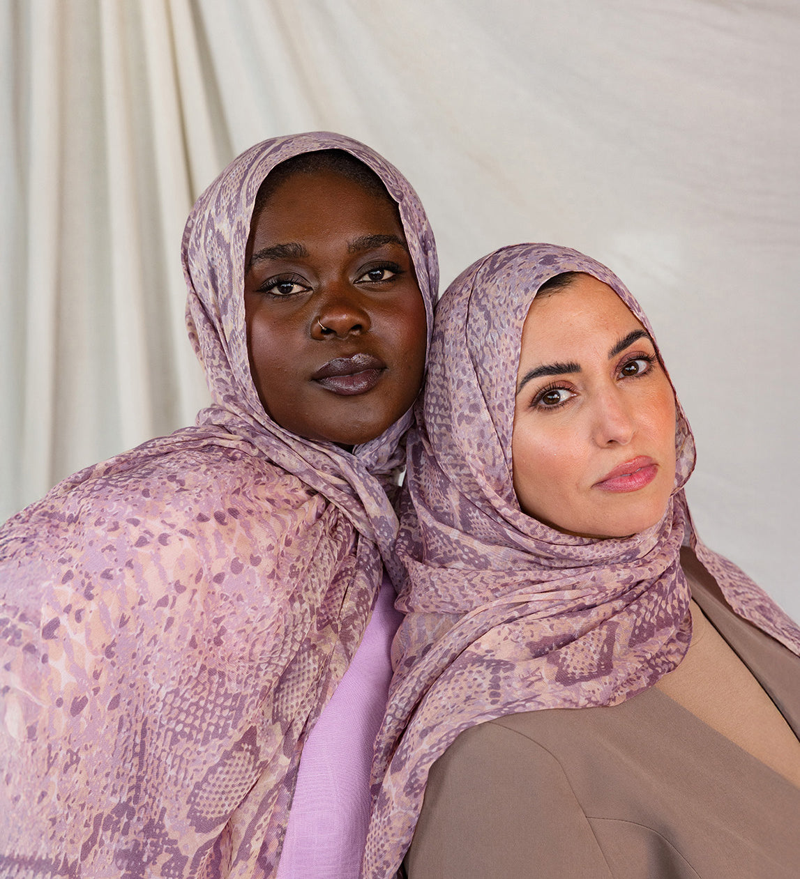 Two models posed together in pink and purple snakeskin print, styled in two different ways.