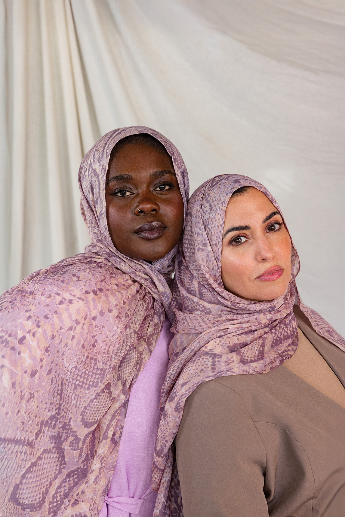 Two models posed together in pink and purple snakeskin print, styled in two different ways.