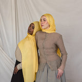 Two models styled in bright yellow hijabs standing against a plain background