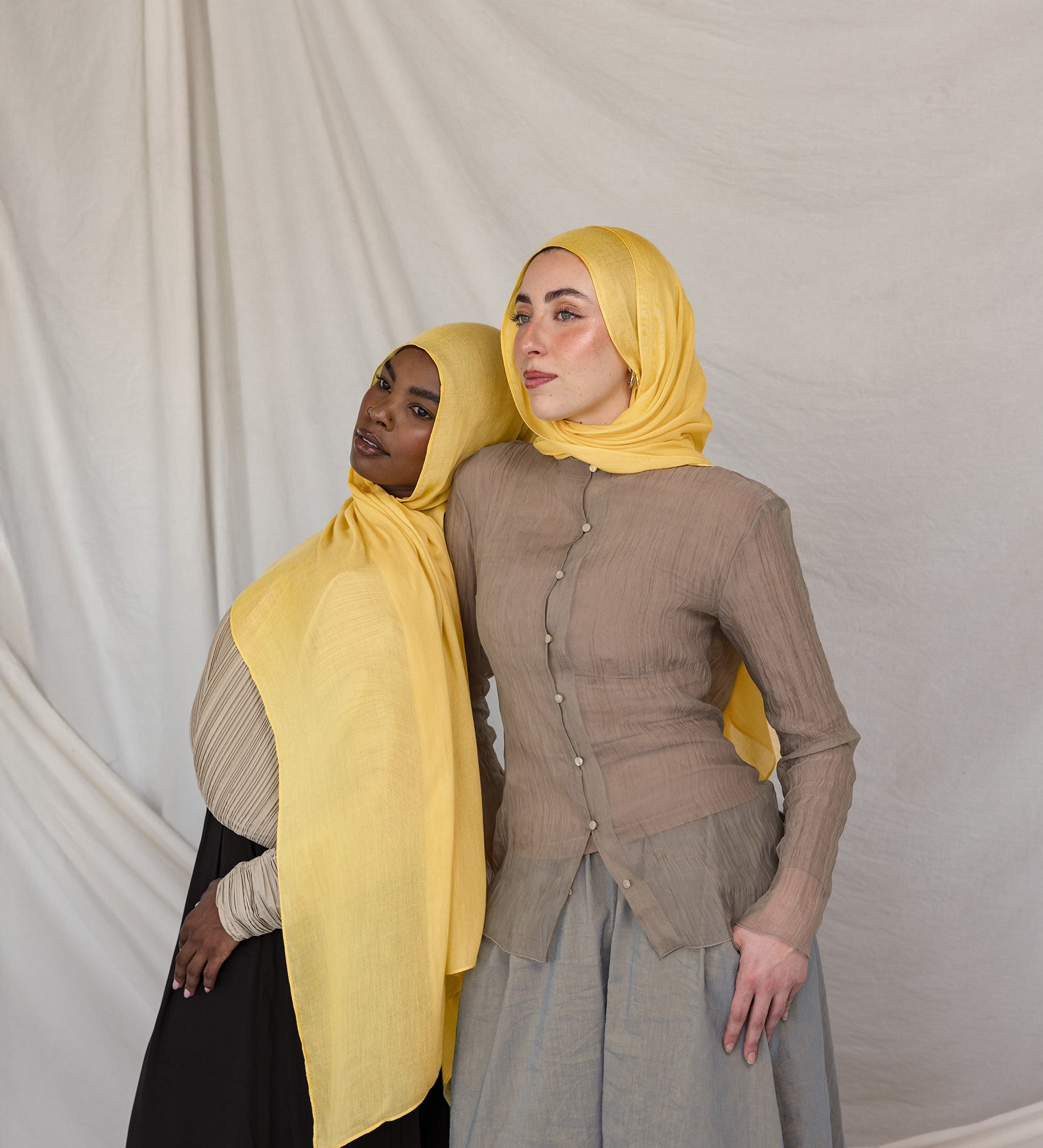 Two models styled in bright yellow hijabs standing against a plain background