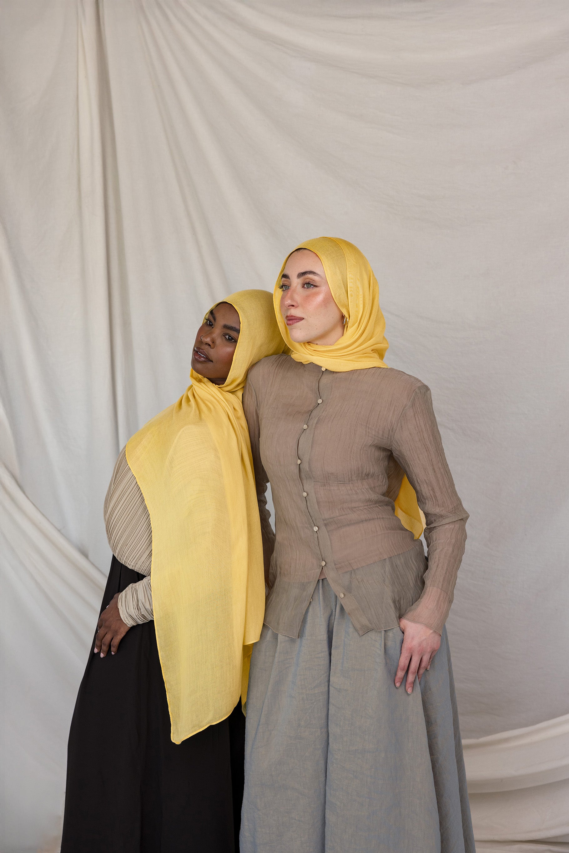 Two models styled in bright yellow hijabs standing against a plain background