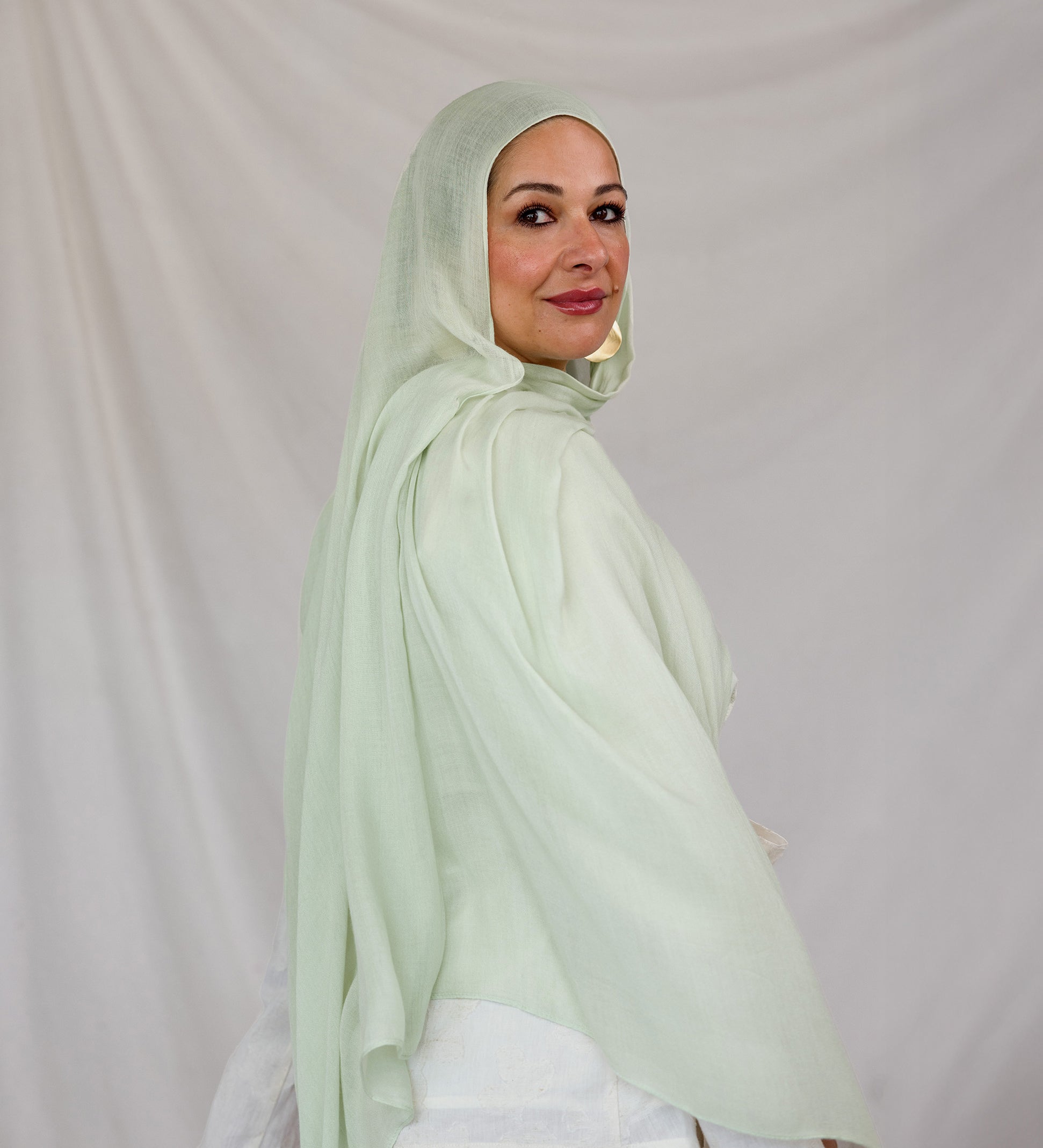 Woman wearing a light pastel green hijab against a plain background