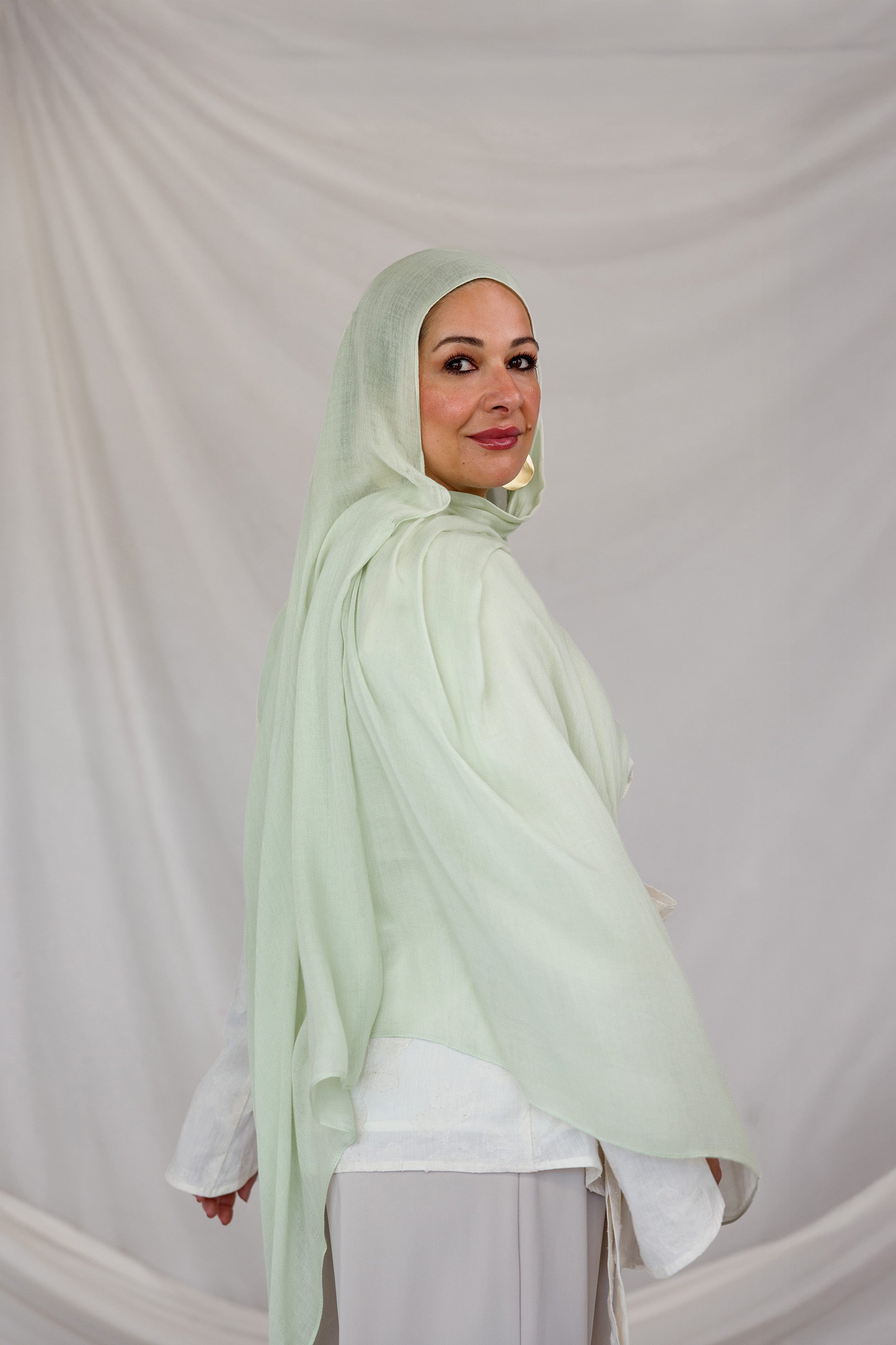 Woman wearing a light pastel green hijab against a plain background