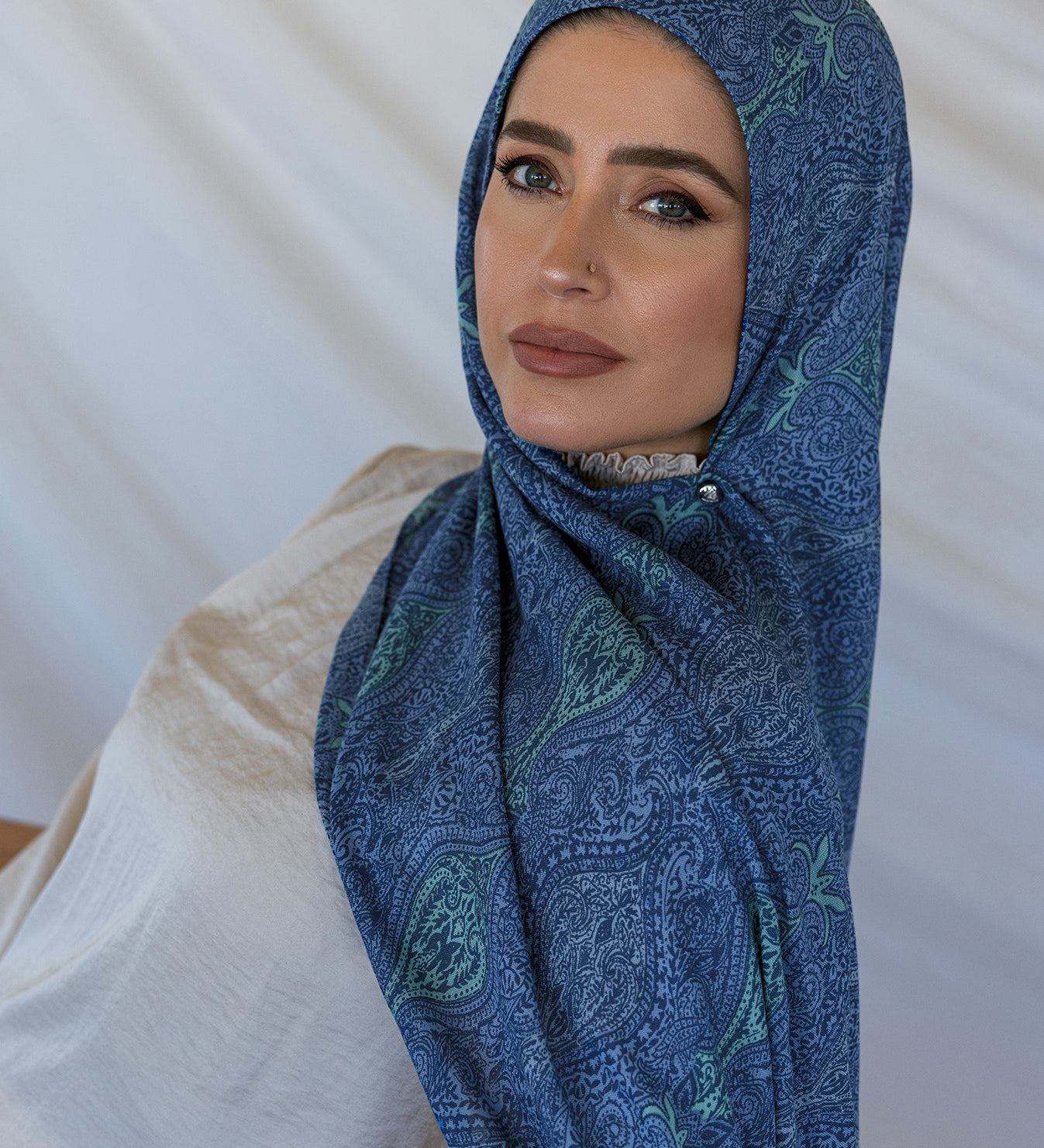 A woman modeling a blue toned paisley print hijab using a hijab magnet.