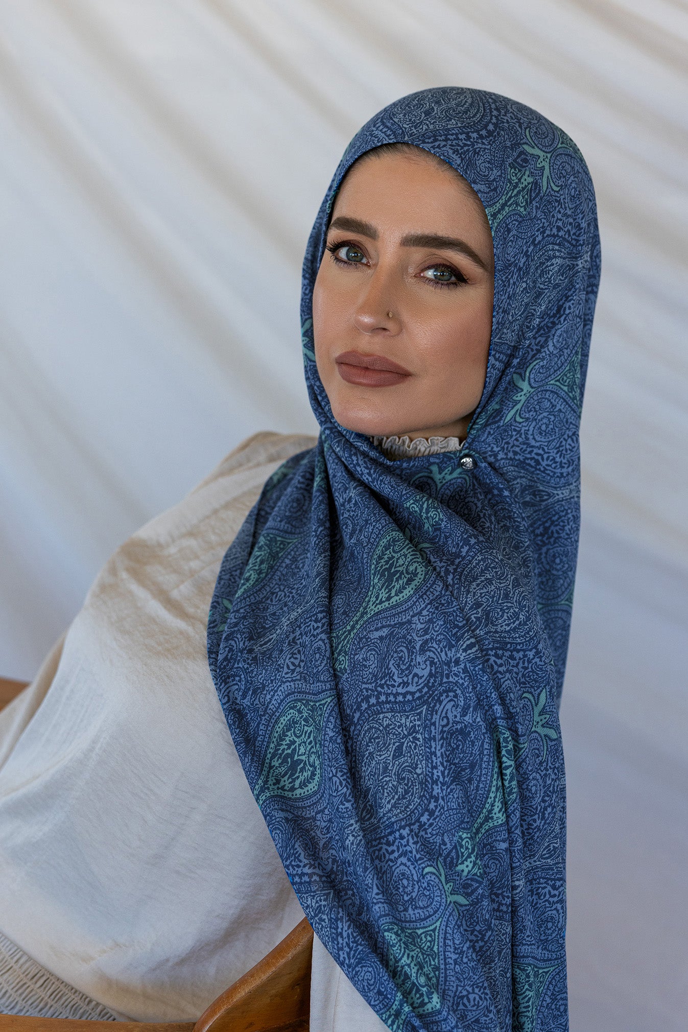 A woman modeling a blue toned paisley print hijab using a hijab magnet.