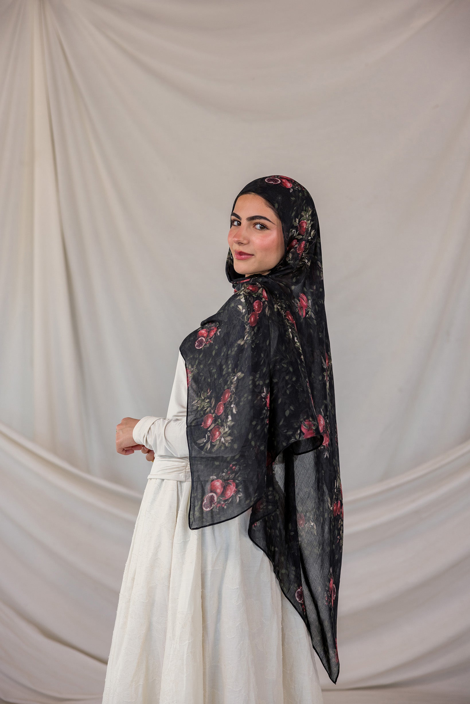 Woman wearing a dark pomegranate print hijab against a plain background