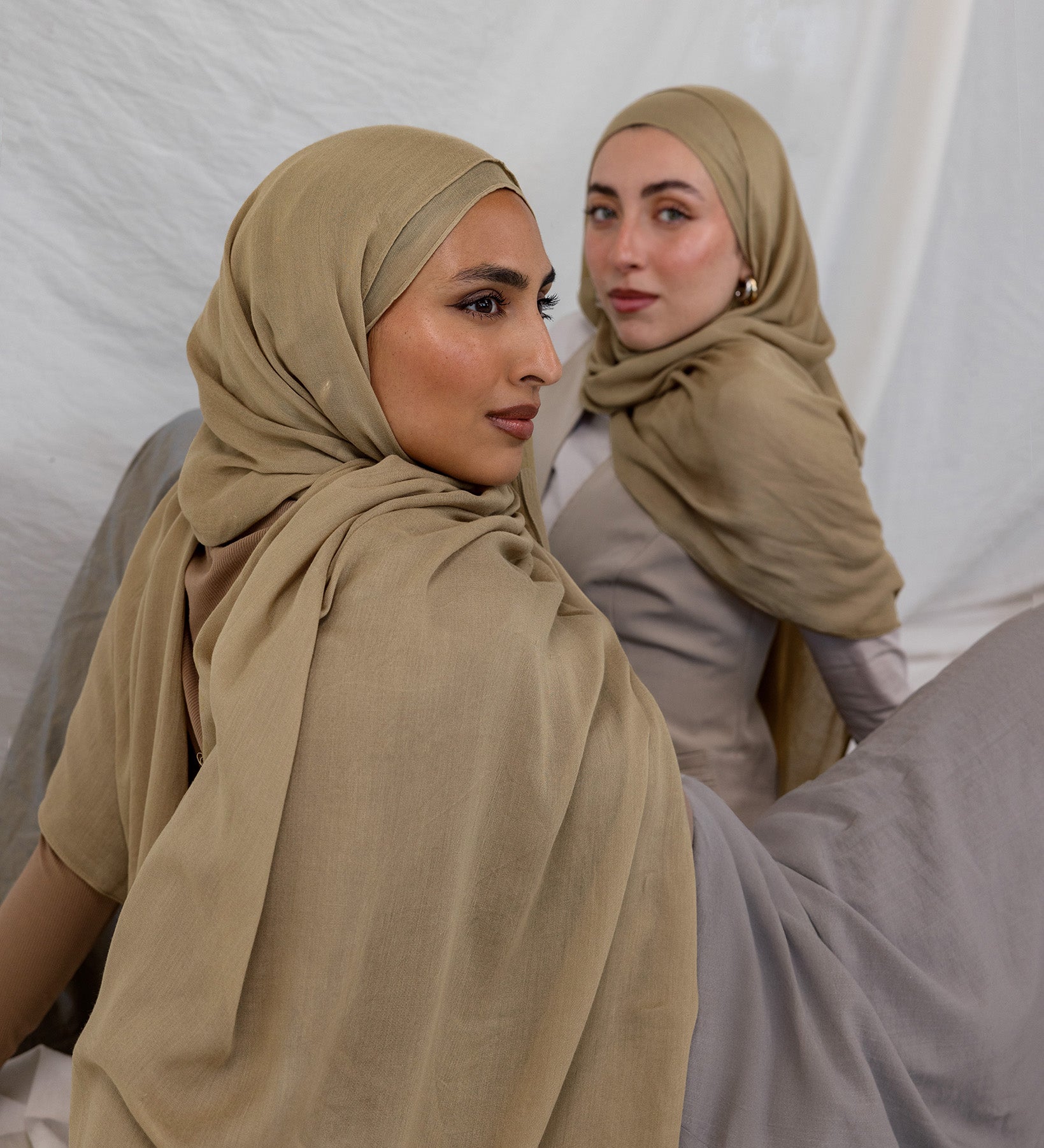 Two models shown wearing the Sandalwood scarf by VELA, which is a neutral, earthy sand color.