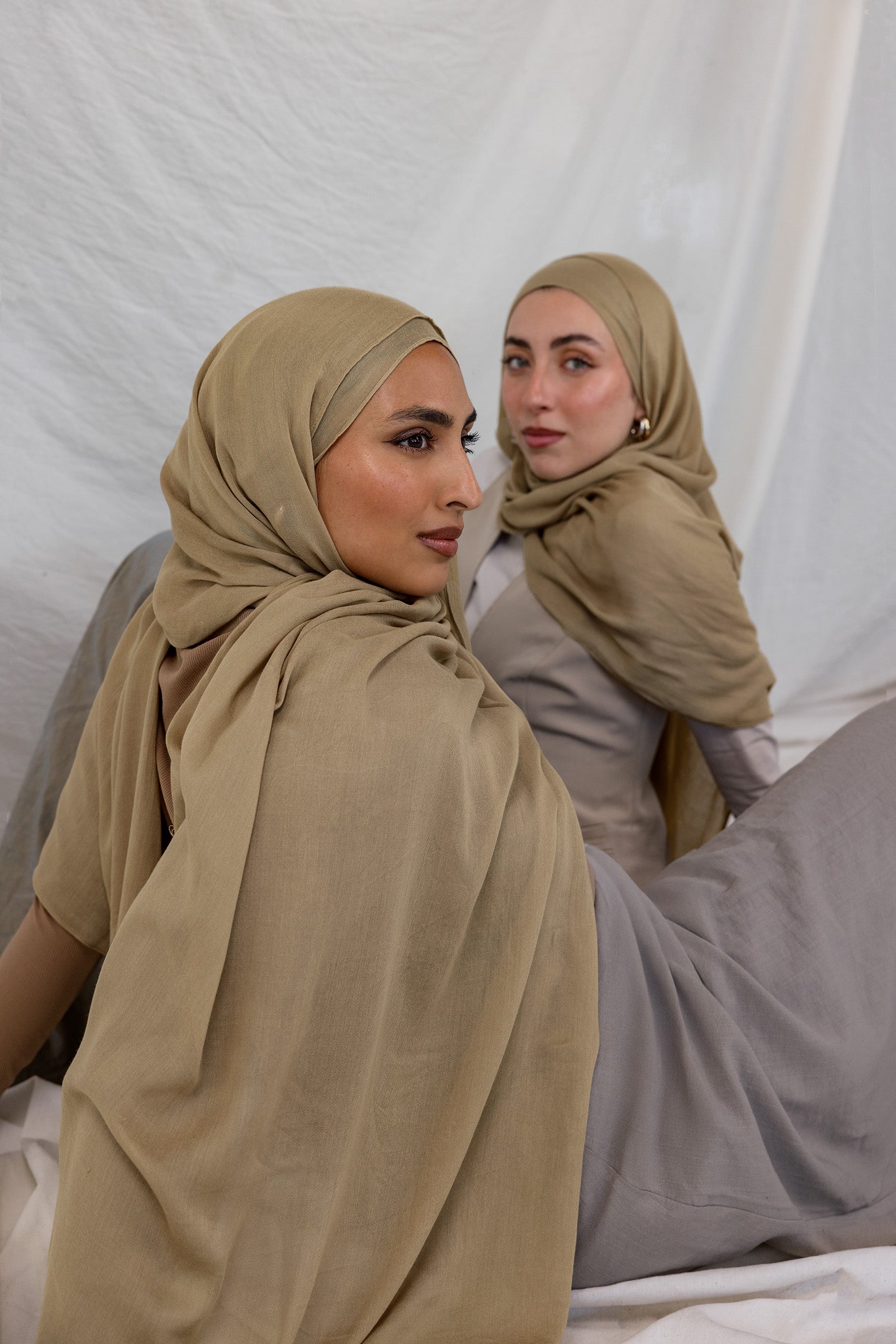 Two models shown wearing the Sandalwood scarf by VELA, which is a neutral, earthy sand color.