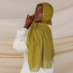 A person wearing a guava green colored hijab with a white outfit.