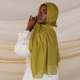 A person wearing a guava green colored hijab with a white outfit.
