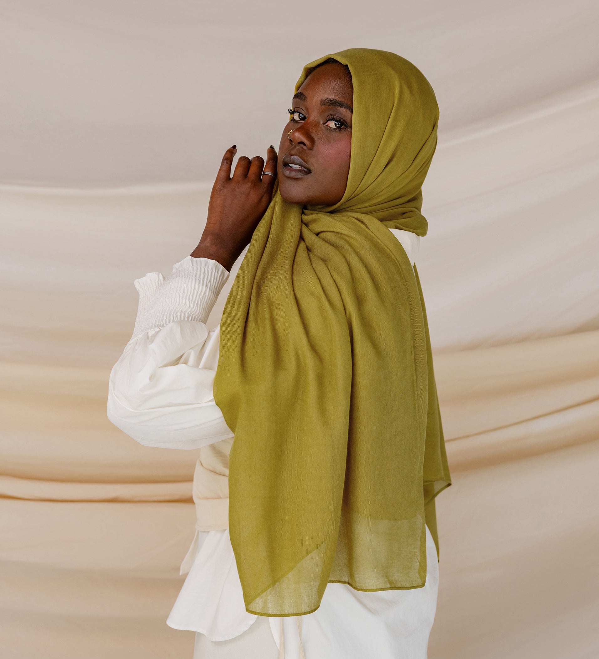 A person wearing a guava green colored hijab with a white outfit.
