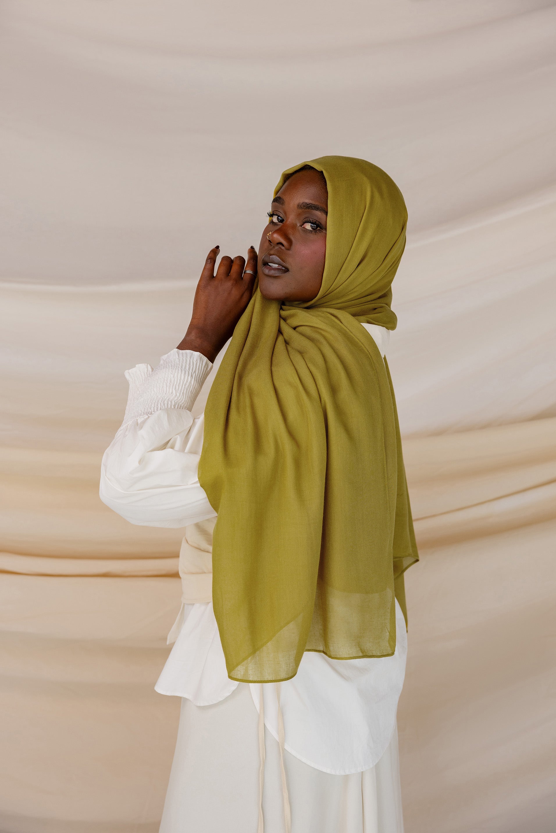 A person wearing a guava green colored hijab with a white outfit.