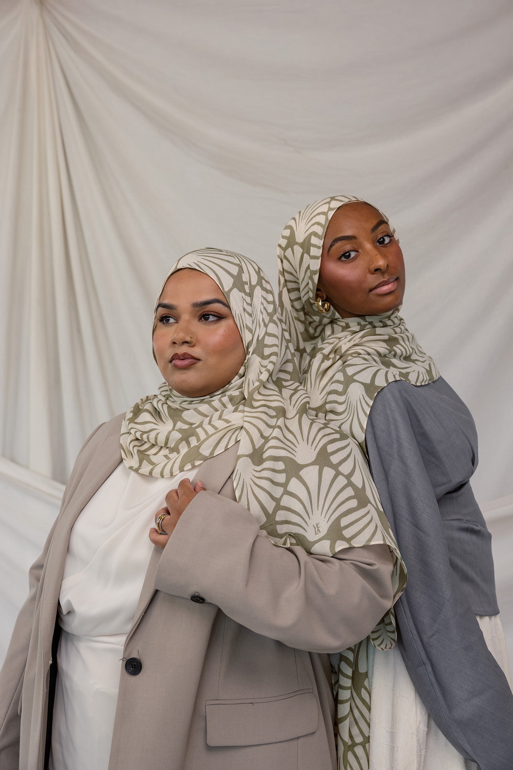 Two women side by side in matching beige and white leaf print hijabs, styled against white background.