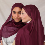 Two models standing side by side wearing the Maroon hijab, styled neatly to frame the face against a neutral studio backdrop.