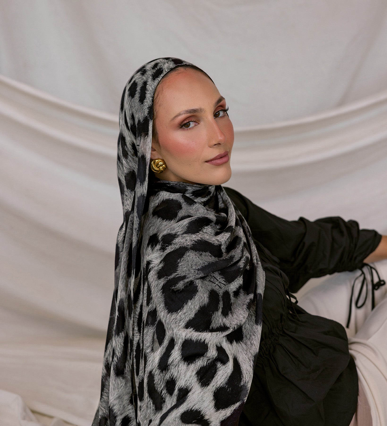 Woman wearing a black and white leopard patterned hijab against a plain background