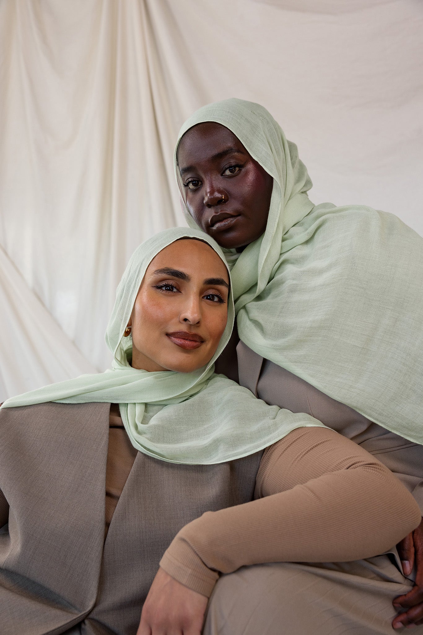 Two women wearing light pastel sea foam green hijabs against a plain background