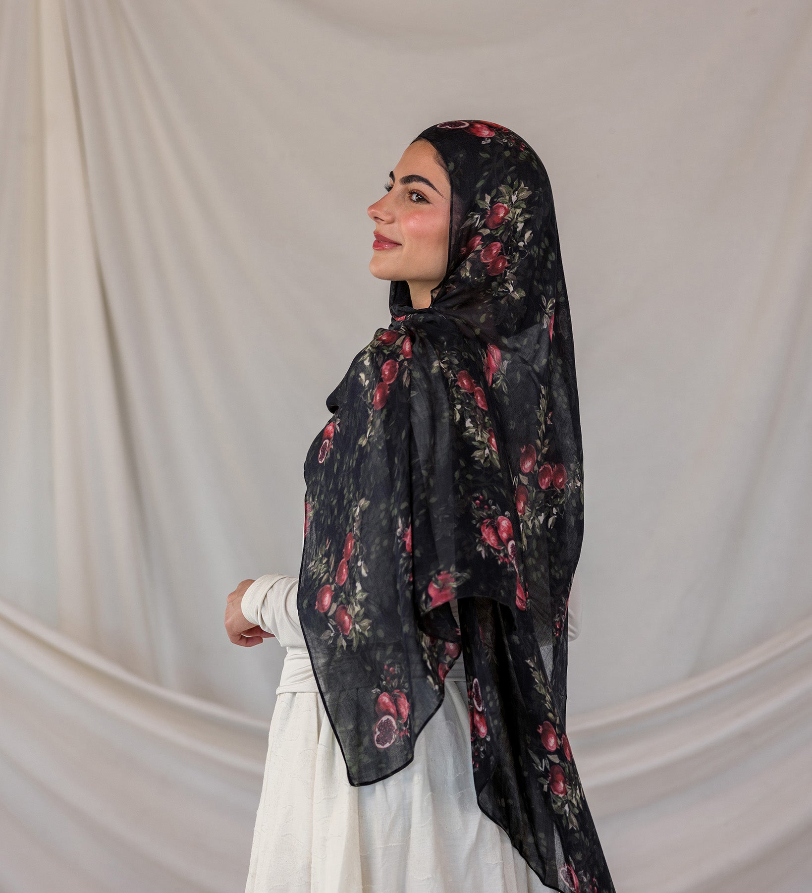 Woman wearing a black pomegranate printed hijab against a plain background