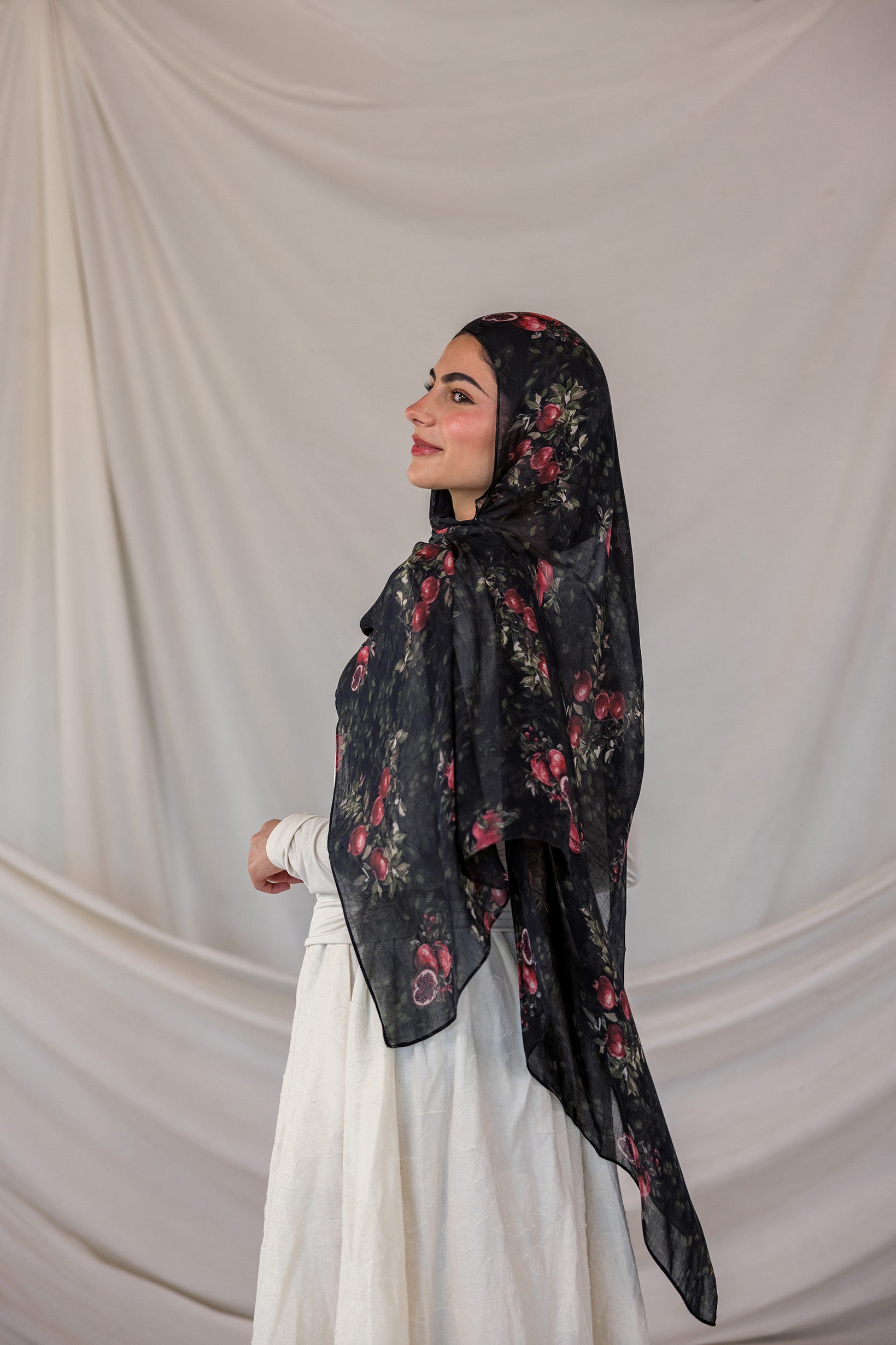 Woman wearing a black pomegranate printed hijab against a plain background