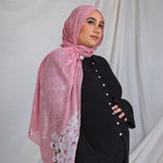 A woman wearing a pink printed hijab featuring cherry blossoms in pink and white.