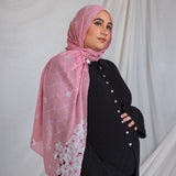 A woman wearing a pink printed hijab featuring cherry blossoms in pink and white.