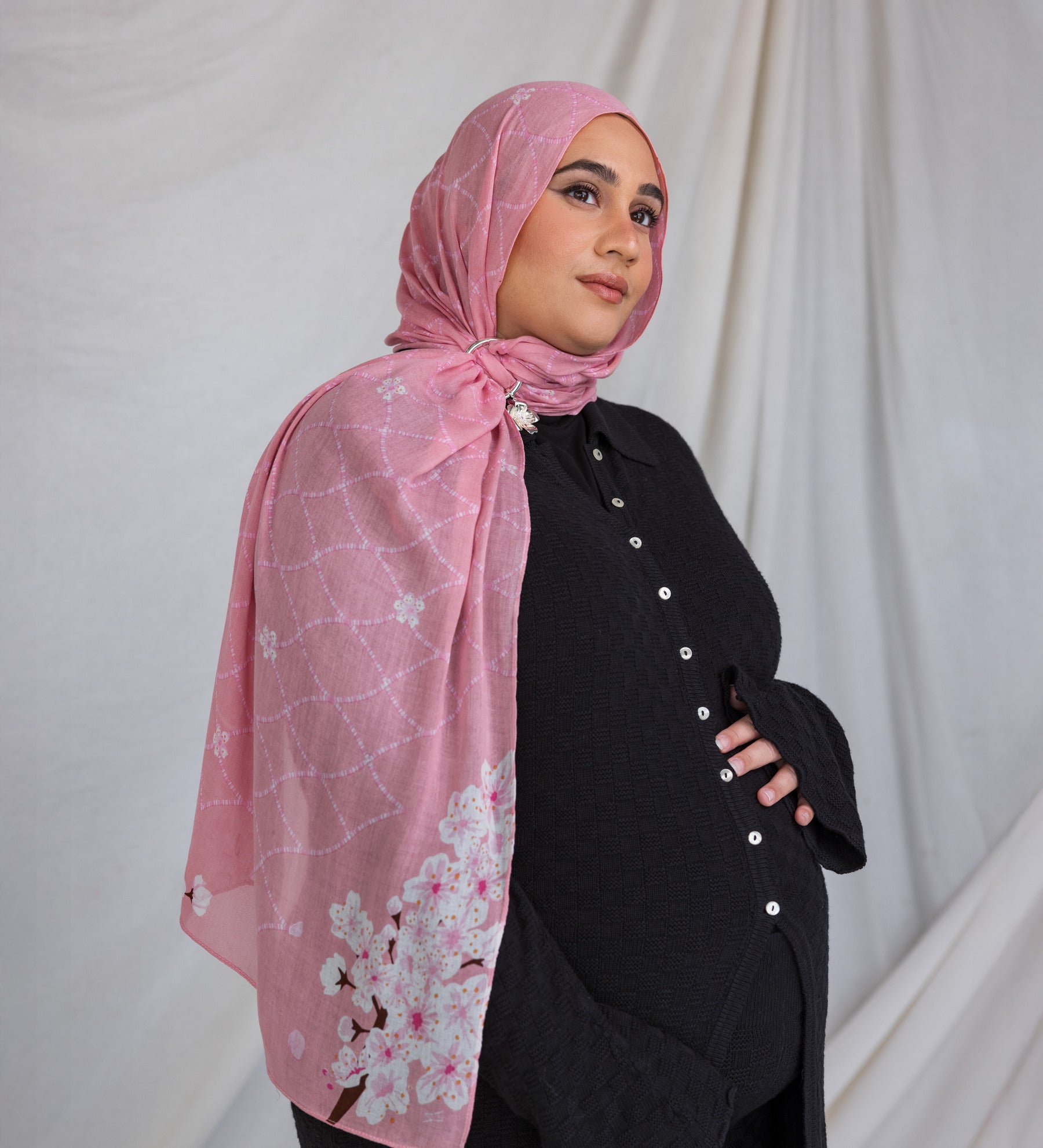 A woman wearing a pink printed hijab featuring cherry blossoms in pink and white.