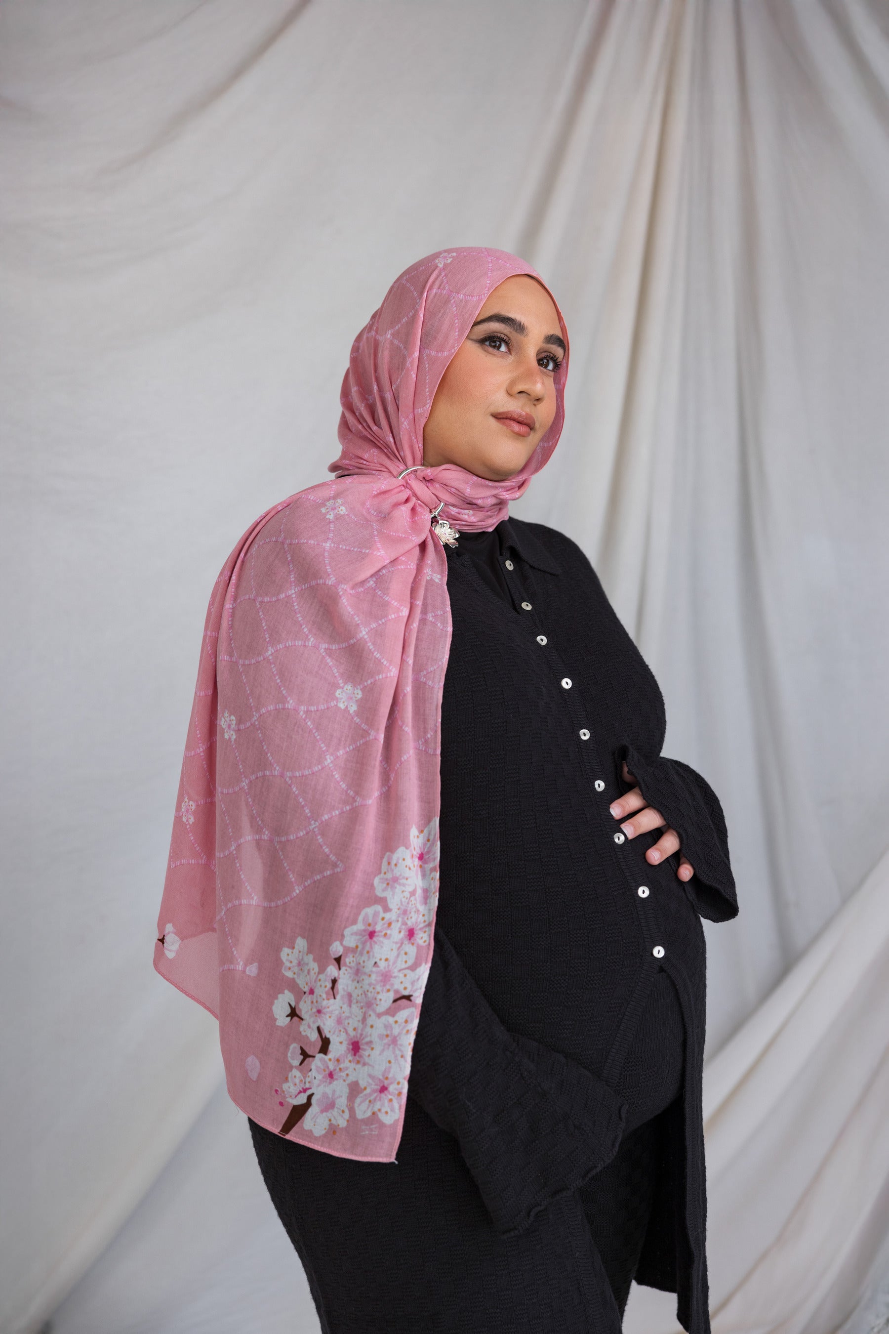 A woman wearing a pink printed hijab featuring cherry blossoms in pink and white.