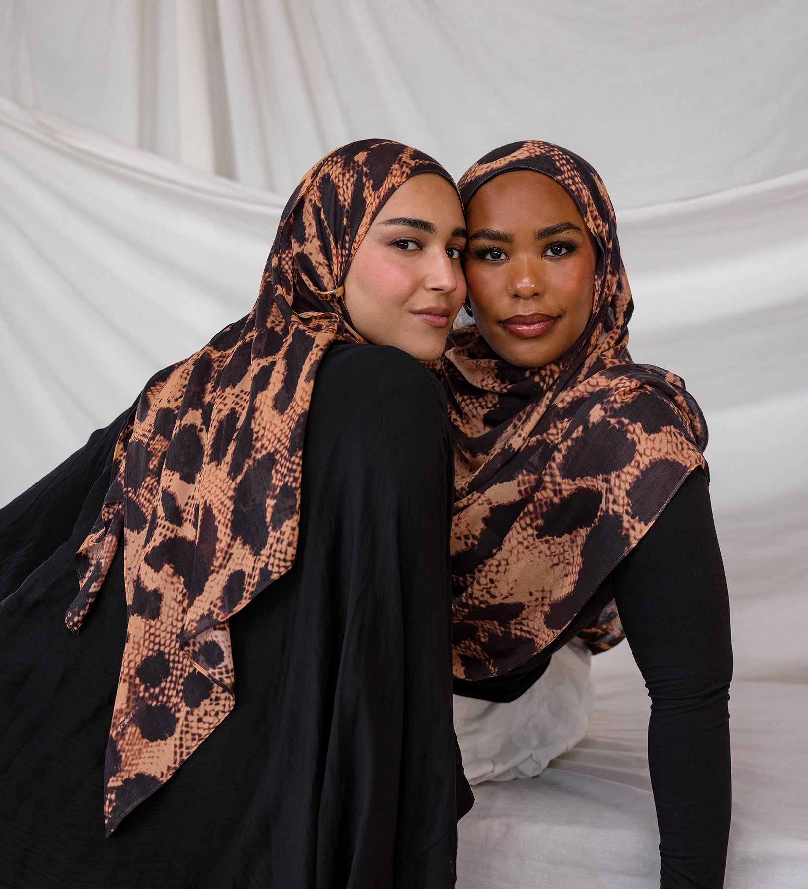 Two models depicted both wearing the Wild Savanna scarf, a peach/tan based scarf with dark spots like an animal, styled in different ways.