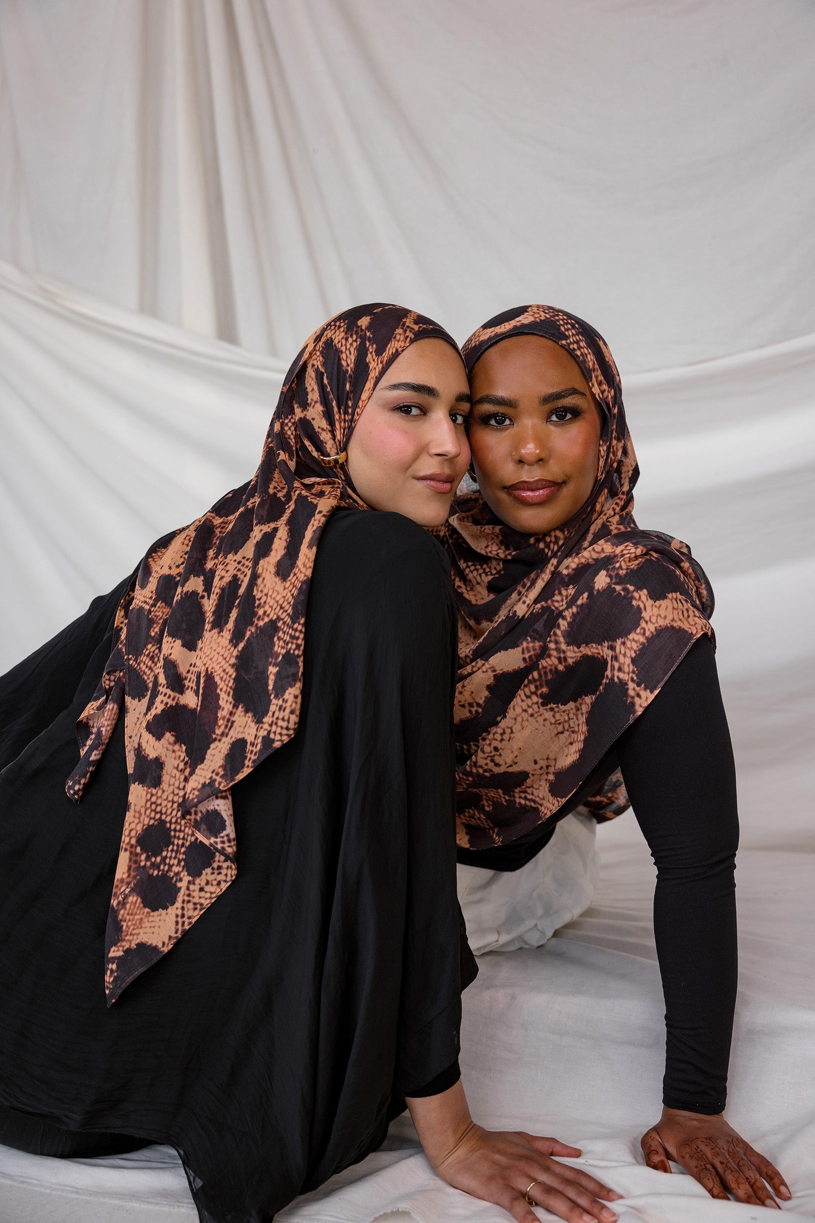 Two models depicted both wearing the Wild Savanna scarf, a peach/tan based scarf with dark spots like an animal, styled in different ways.