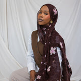 A woman wearing a brown printed hijab with pink and white cherry blossoms.