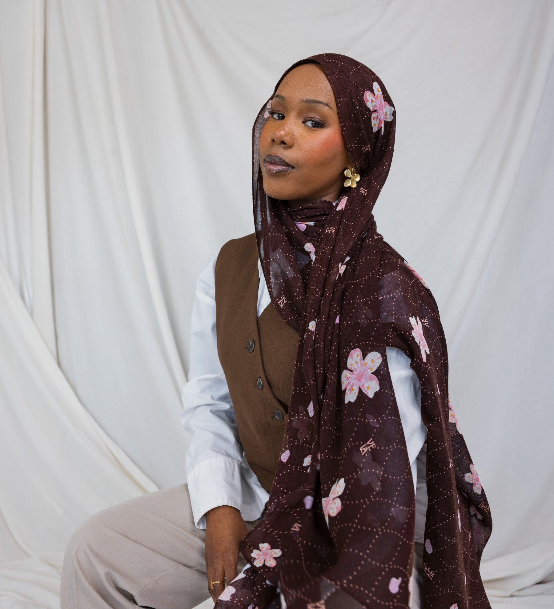 A woman wearing a brown printed hijab with pink and white cherry blossoms.