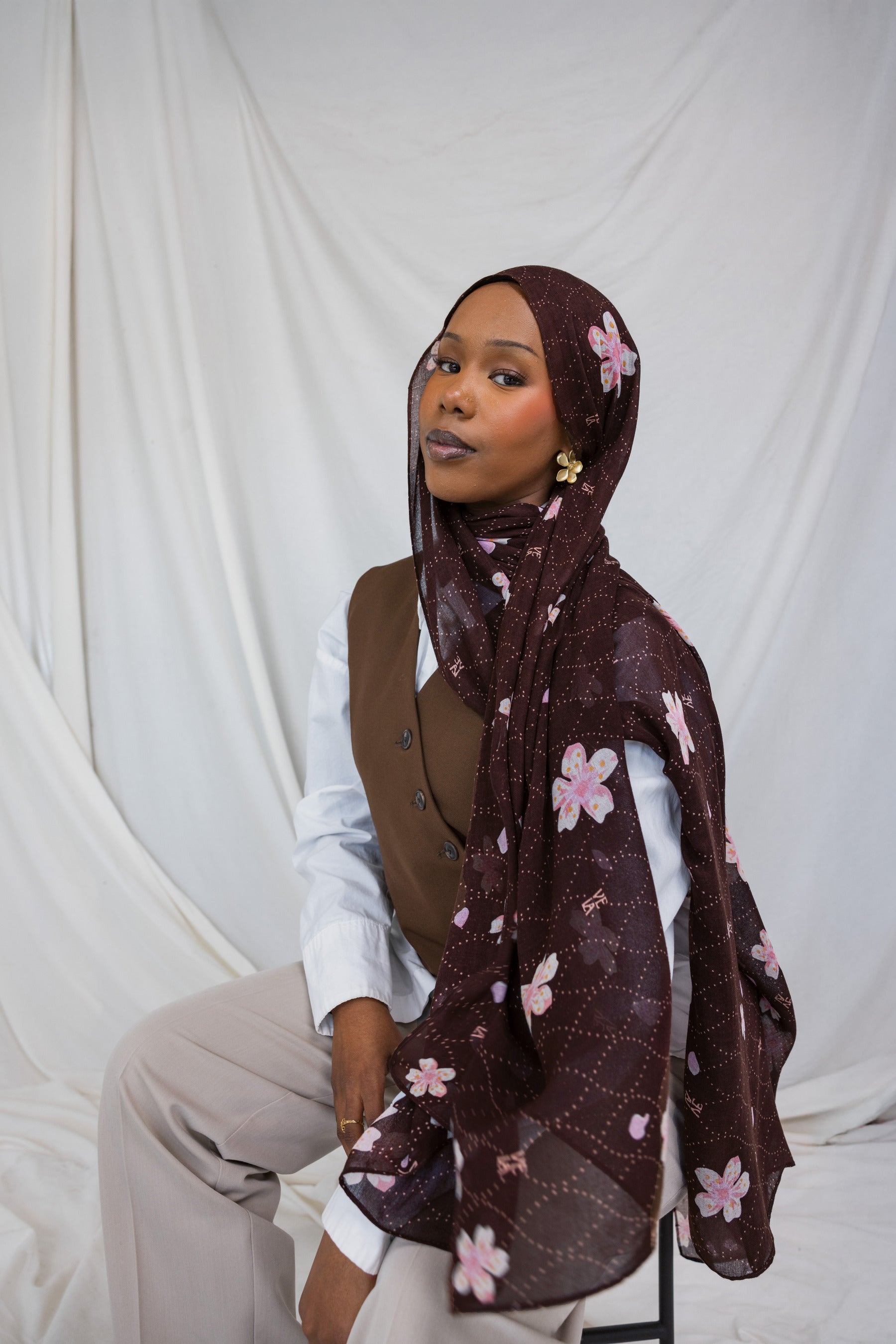 A woman wearing a brown printed hijab with pink and white cherry blossoms.
