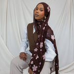 A woman wearing a brown hijab printed with pink and white cherry blossoms.
