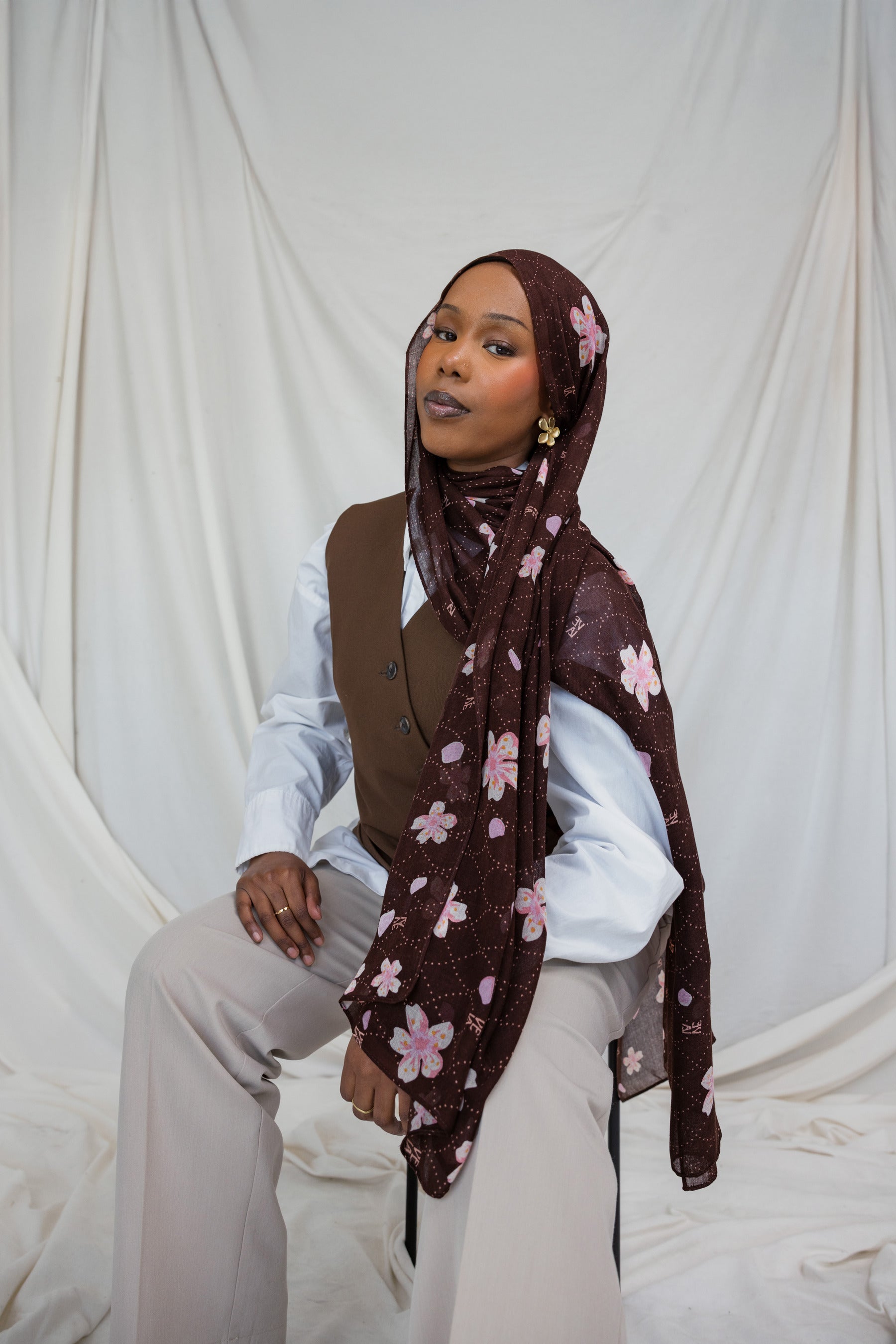 A woman wearing a brown hijab printed with pink and white cherry blossoms.