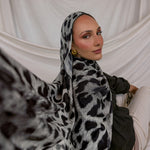 Woman wearing a leopard print hijab against a white draped background