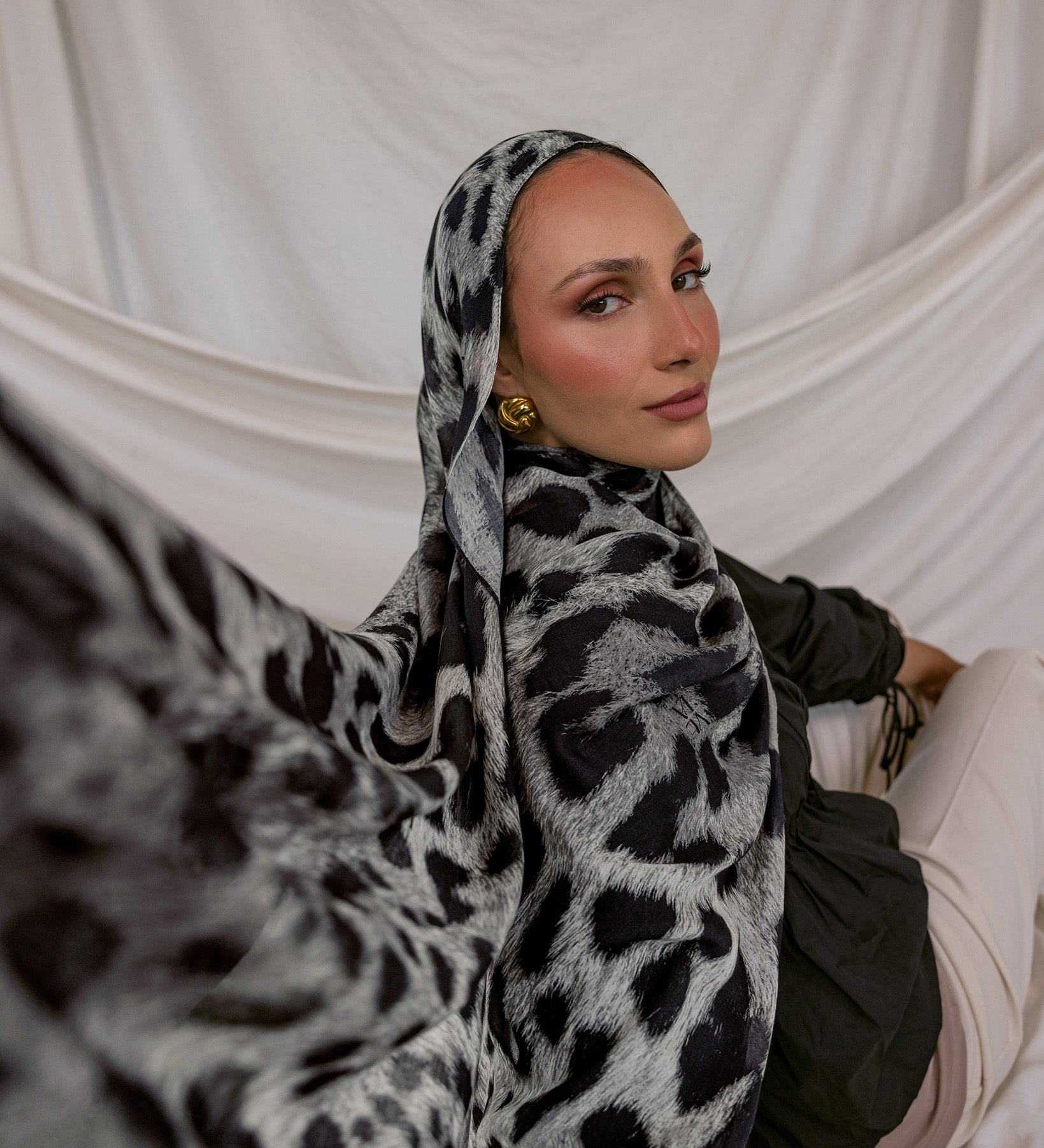 Woman wearing a leopard print hijab against a white draped background