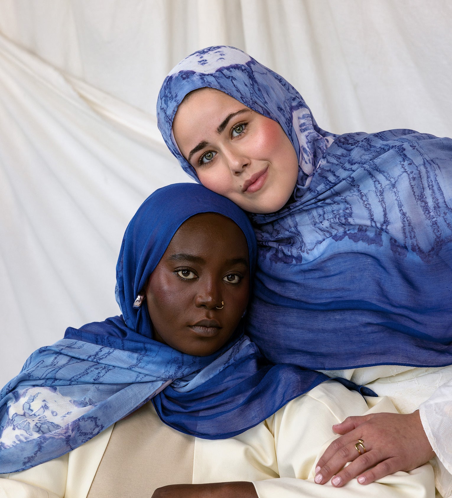 Two women wearing blue with white shell printed hijabs against a white background
