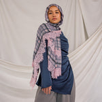 Woman wearing a blue outfit with a pink checkered plaid patterned scarf against a plain background