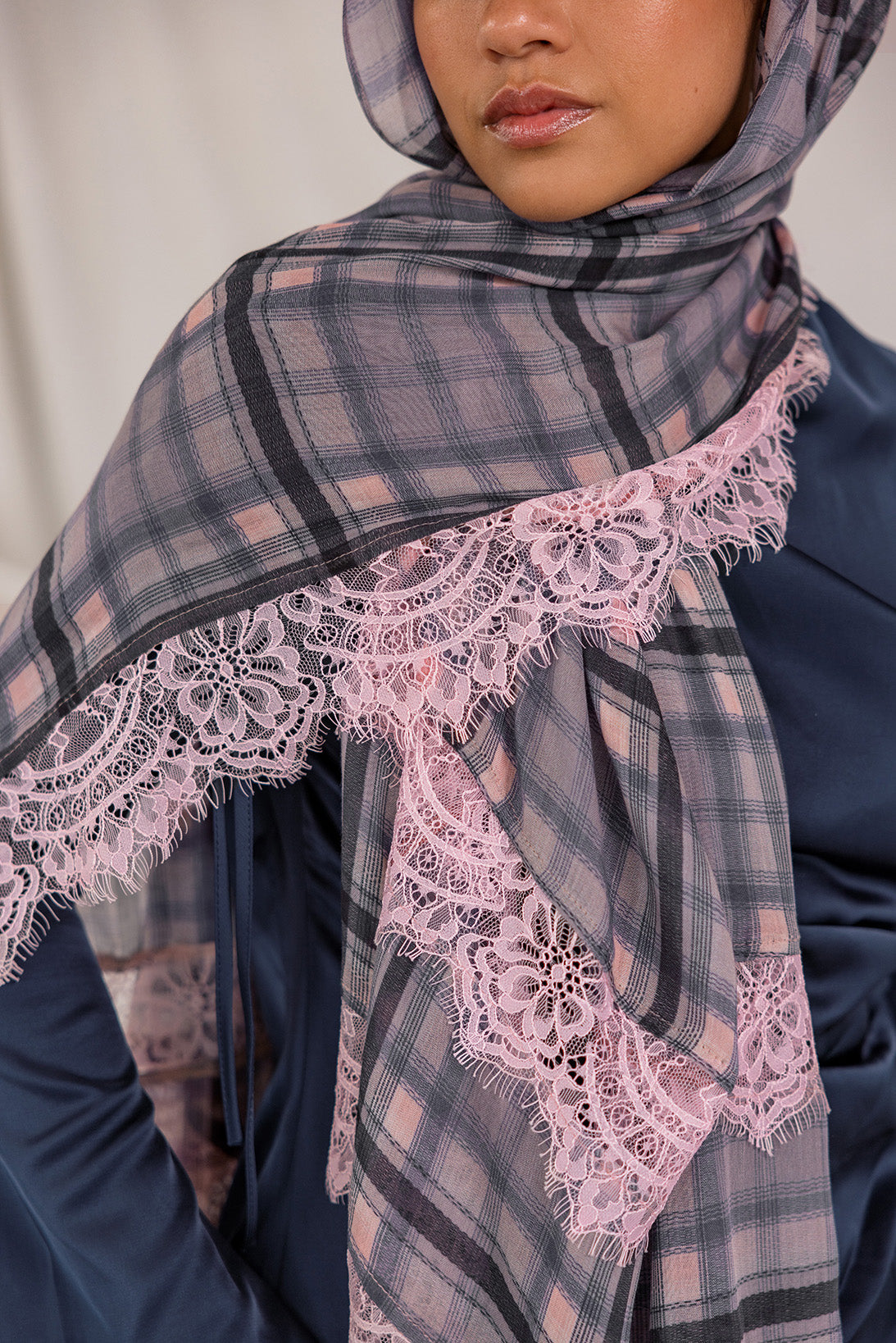 Model styled in a plaid scarf with lace trim over a dark blue outfit.