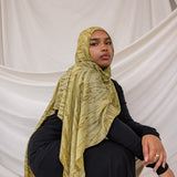 Model wearing a olive printed dune hijab and black outfit against a white draped background