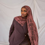 Model wearing a red clay ripple patterned hijab and dark clothing against a plain background