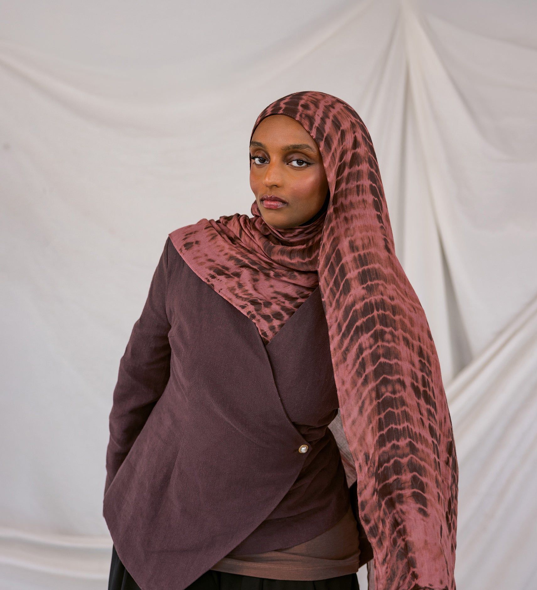 Model wearing a red clay ripple patterned hijab and dark clothing against a plain background