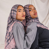 Two women wearing patterned pink plaid hijabs and gray tops against a plain background