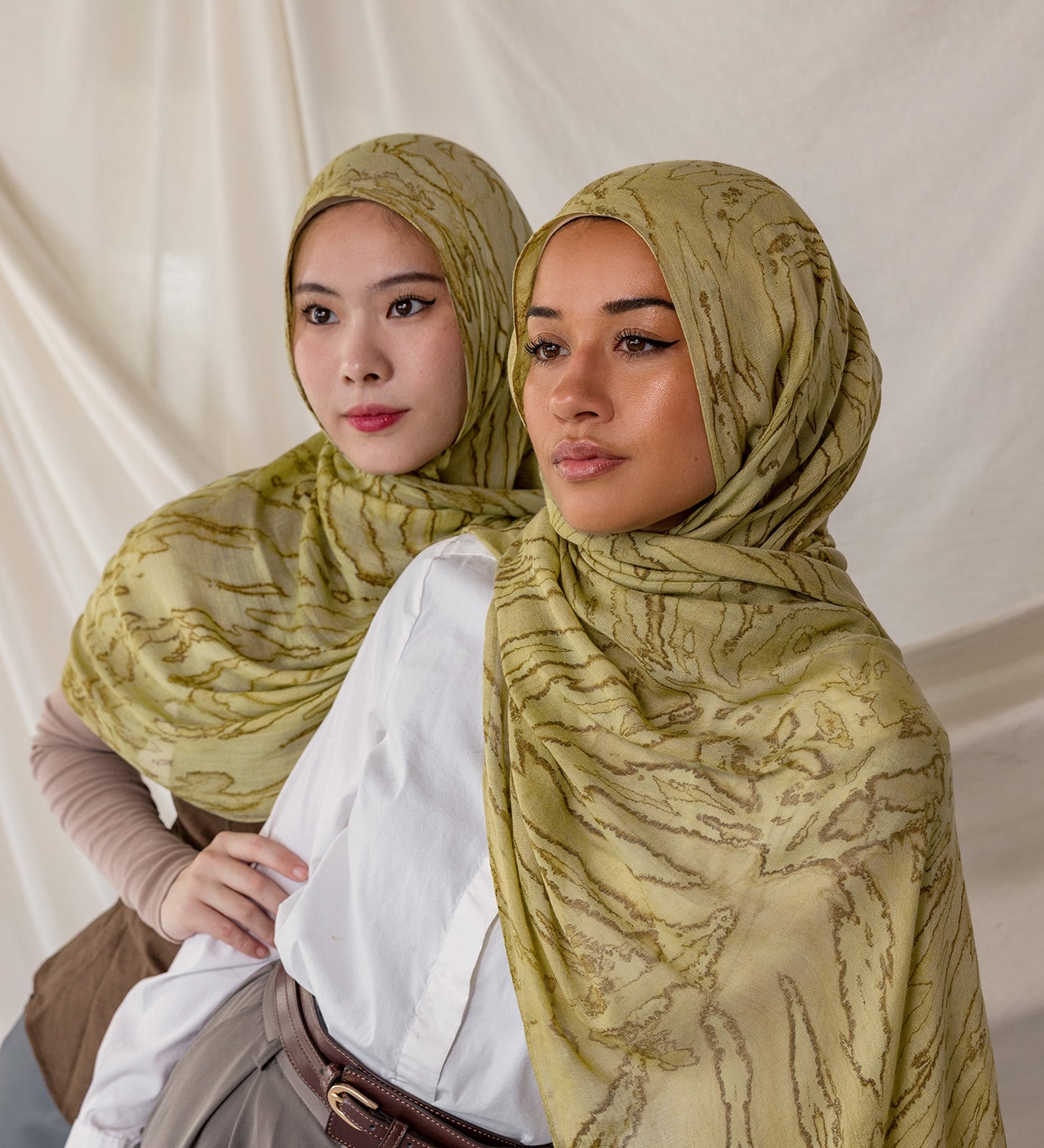 Two women styled in green printed dune hijabs against a plain background.